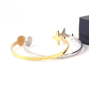 Detail of travel the world engraving and airplane charm on stainless steel cuff bracelets