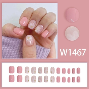 Detail view of pink press-on nails with white flower patterns and golden accents, model W1467