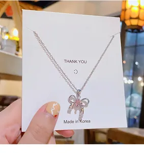 Détail du collier noeud argenté avec cristal coeur rose sur carte d'affichage