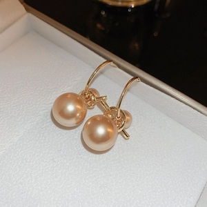 Vue macro de boucles d'oreilles nœud doré avec perles champagne dans un coffret blanc