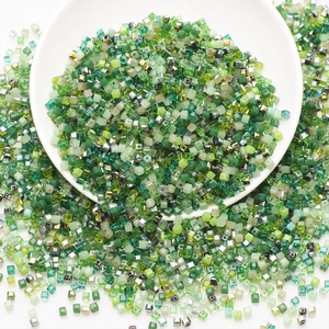 Detailed top view of bulk green square glass beads in a white bowl for DIY jewelry