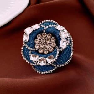 Detail of blue denim flower brooch with rectangle rhinestones on silk background