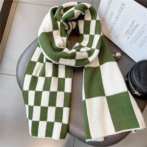 Flat lay of green and white checkerboard knit scarf on a leather cushion with decor