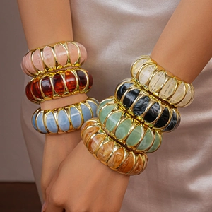 Close-up of chunky gold-tone bangles with colorful marble-effect resin inlays and texture