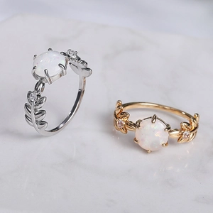 Dettaglio di anelli in oro e argento con foglie, opale bianco e pietre di zircone