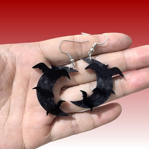 Halloween acrylic black bat and moon earrings shown on a hand with red gradient background