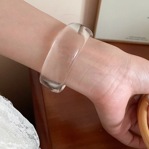 Close-up of a wide transparent resin geometric open bangle on a female wrist