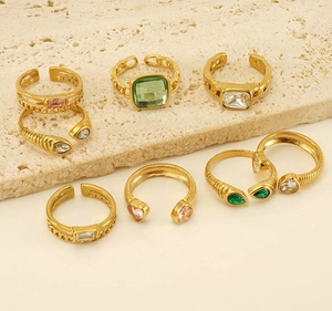 Detailed shot of gold-plated rings with colorful gemstones on a beige stone surface