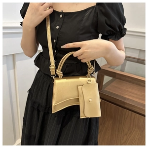 Détail du sac à main sablier doré mat avec base incurvée et pochette suspendue assortie