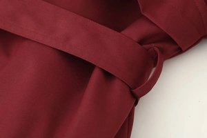 Détail du trench-coat bordeaux montrant le tissu en sergé et les coutures de la ceinture