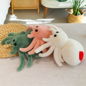 Three soft plush spider toys in green, pink, and white stacked on a cozy sofa