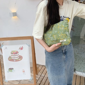 Close-up of floral embroidery on a green fabric pouch held by a model in daylight