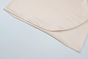 Detail shot of beige dress featuring curved layered design and fine knitted texture