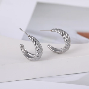 Détail des boucles d'oreilles créoles torsadées argentées en forme de C sur support moderne