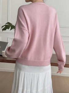 Rear view of a loose-fit pink long-sleeved knit sweater featuring ribbed hem and cuffs
