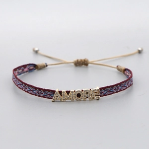Close-up of woven boho bracelet featuring AMORE gold letter charm with crystal stones