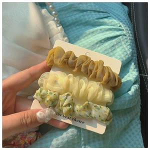 Detailed view of three yellow floral chiffon scrunchies on white card packaging