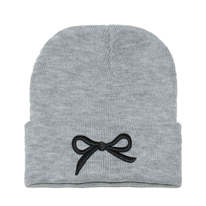 Détail du bonnet en maille grise avec un nœud noir brodé texturé sur le revers de la tête