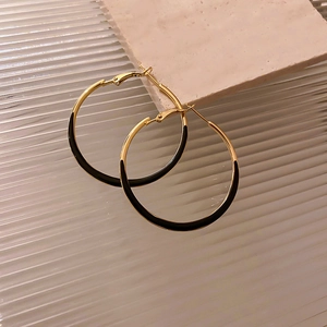 Close-up of geometric hoop earrings featuring gold metal and black enamel finish
