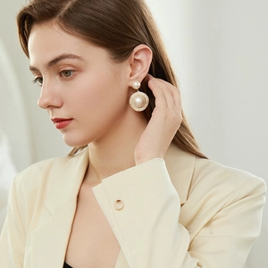Close-up of oversized pearl earrings with gold base and rhinestones on a model