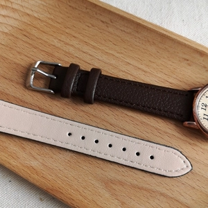 Detail of quartz watch with dark brown and beige leather straps on light wooden tray
