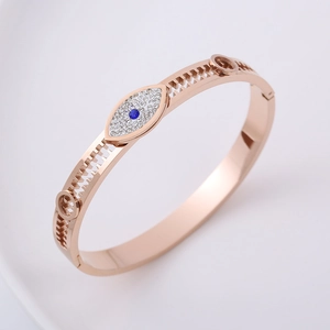 Detail of rose gold gear-edged bangle featuring a crystal-encrusted evil eye motif
