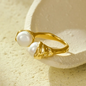 Minimalist gold open ring with lava texture and two white pearls on a ceramic dish