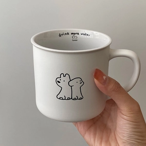 Minimalist white ceramic puppy mug held by hand with drink more water print inside
