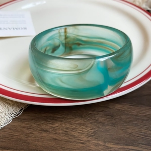 Detailed view of acrylic resin bangle with blue and brown marble texture on a white plate