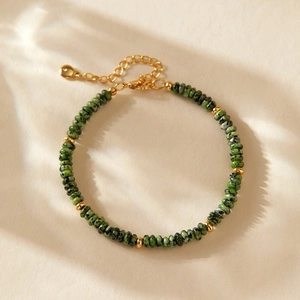 Nahaufnahme von grünen Natursteinperlen und vergoldetem Armband mit Baumschatten-Effekt