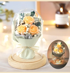 Detail of yellow soap roses and LED lights inside a clear glass dome on wooden base