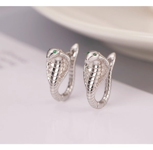 Macro view of silver cobra hoop earrings featuring detailed scales and green gemstone eyes