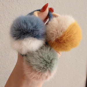 Dettaglio di tre elastici per capelli con pompon di peluche in sfumature rosa, giallo e blu