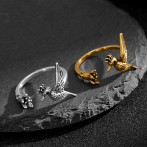 Detailed close-up of hummingbird and flower open ring in silver and gold finishes