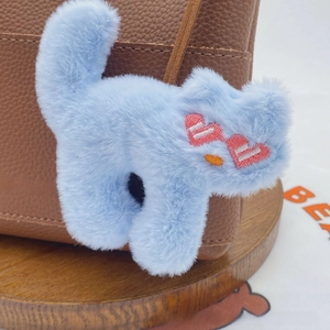 Close-up of a blue plush cat charm with heart sunglasses on a leather handbag