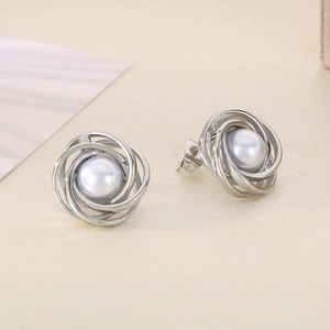 Macro detail of silver spiral earrings featuring elegant grey pearl center on textured fabric
