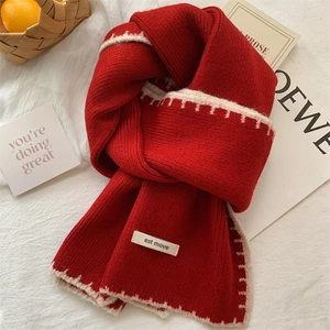 Detail of red knit wool scarf with contrast white stitched edges and fabric label
