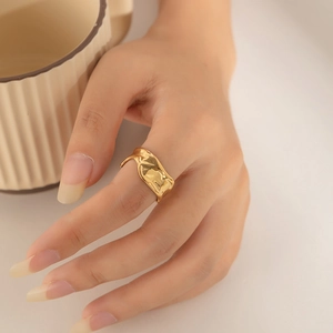 Detail of gold geometric ring with irregular pleated texture on hand against soft background