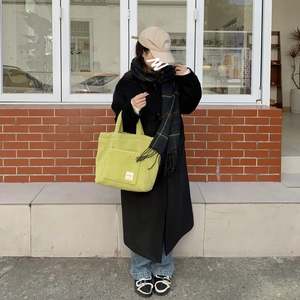 Large green sherpa tote bag styled with a wool coat and casual streetwear on a city street