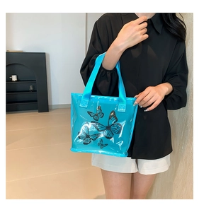 Close-up of a blue transparent PVC tote bag with black butterfly prints and webbing handles