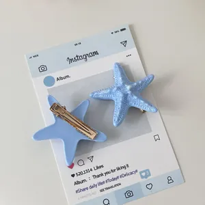Detail of two sky blue starfish hair clips with gold metal grips on a white background