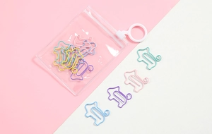 House-shaped colorful paper clips in a transparent bag on a pastel pink background