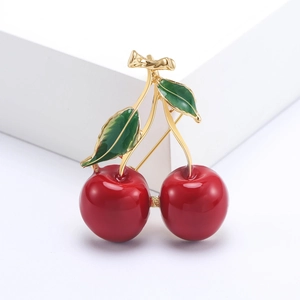 Charming red cherry brooch with golden base and green leaves on minimalist background