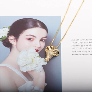Golden ram pendant necklace with pavé cubic zirconia and green gem eyes on a book