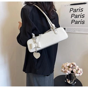 Detail of white leather baguette bag featuring a large bow and silver heart pendant