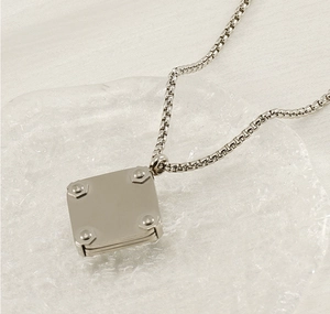 Close-up of a silver industrial square rivet pendant on a textured glass base