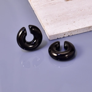 Close-up of a glossy black C-shaped chunky ear cuff on a minimal lilac mirror background