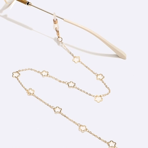 Detailed close-up of golden eyewear chain featuring white floral charms and fine alloy links