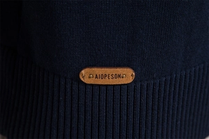 Gros plan sur la maille bleu foncé avec étiquette logo en cuir sur l'ourlet côtelé