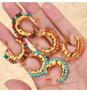 Detail of gold C-shaped earrings with colorful natural beads held by hand for size scale
